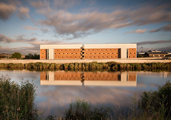 View of block of buildings from across the river. Attractive wooden and concrete structure bathed in afternoon sunlight.